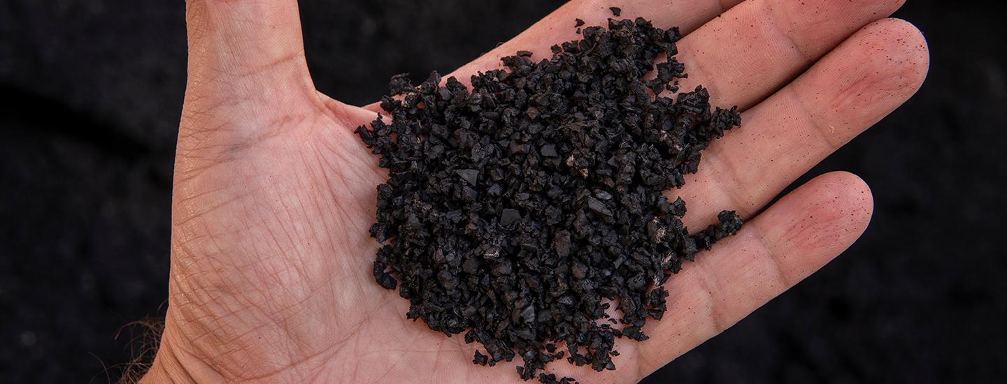Close-up of recycled rubber pellets held in a hand, showing texture.
