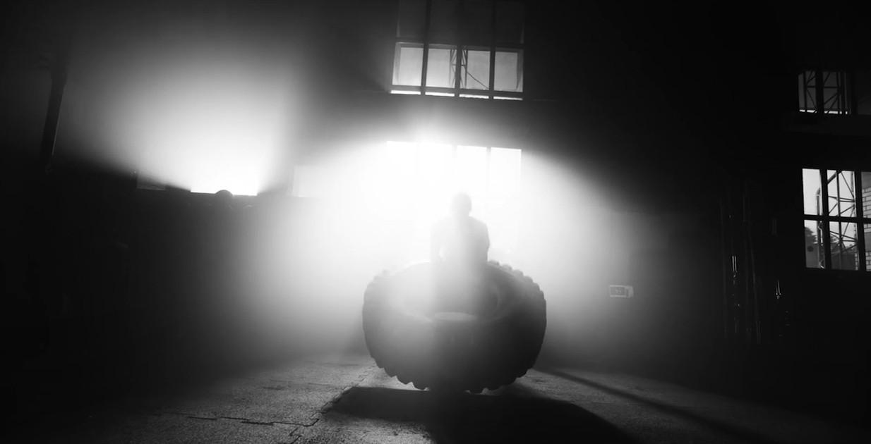 A man in a dimly lit gym flipping a large tire working out on Ecore Athletic flooring